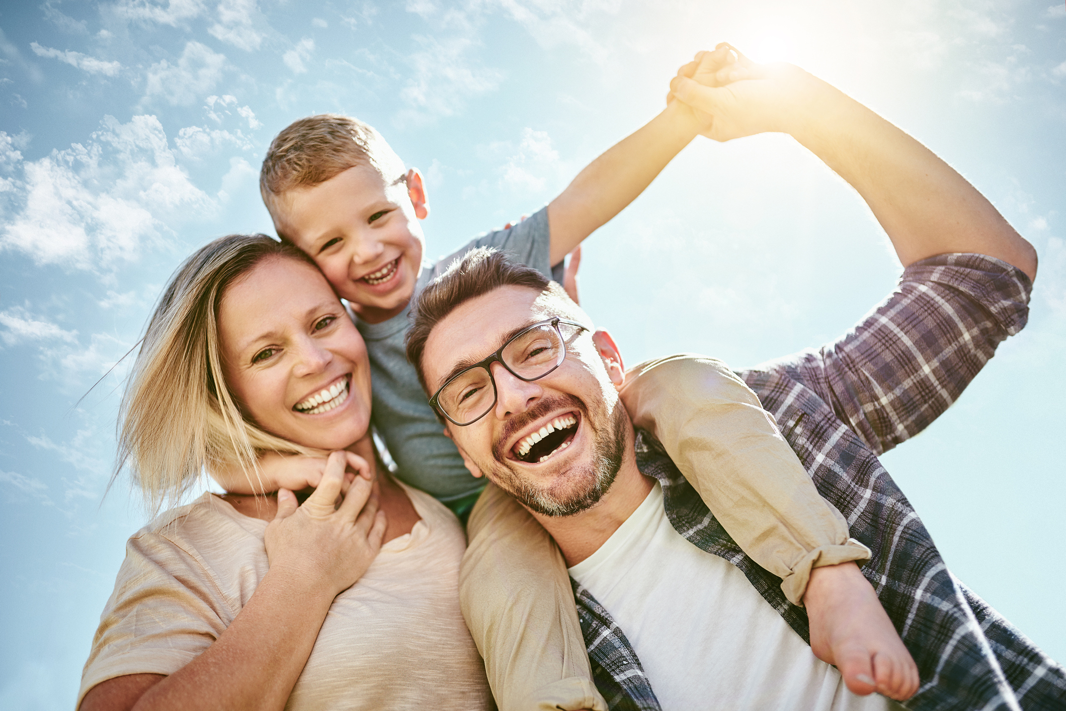 Happy Familly - Mother, Father and Little Boy whos is sitting the father's shoulders outside in the sun. 